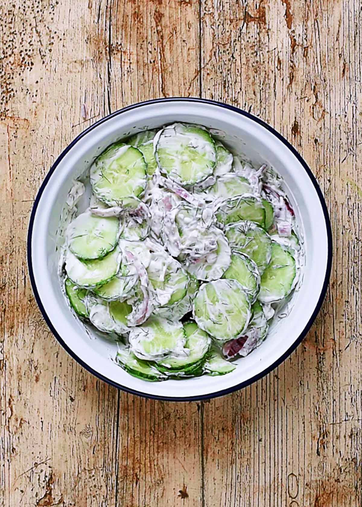 Sliced cucumber mixed in a bowl with onion, cream and dill.