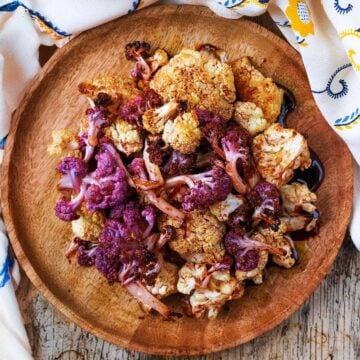 Garlic roasted cauliflower on a round wooden plate.