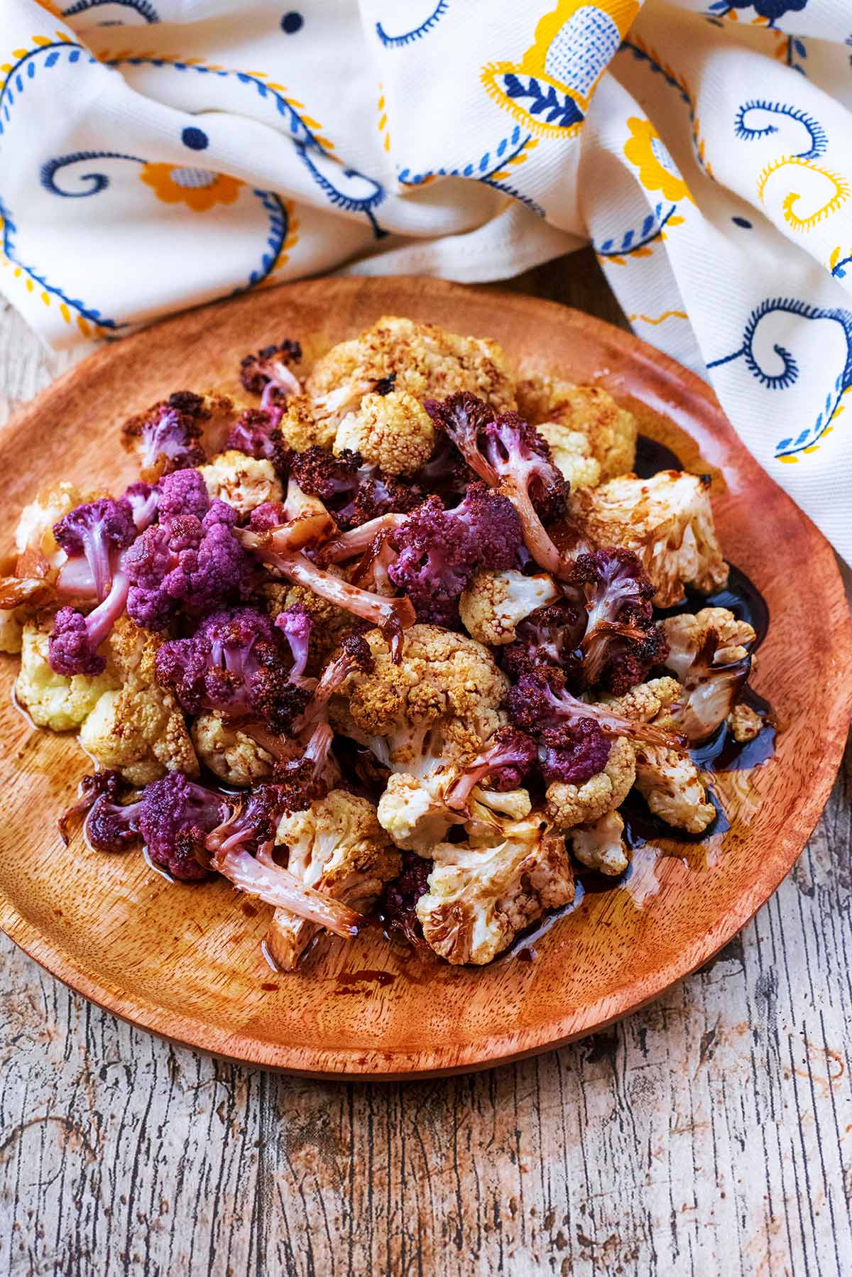 Roasted cauliflower florets on a round wooden serving plate.