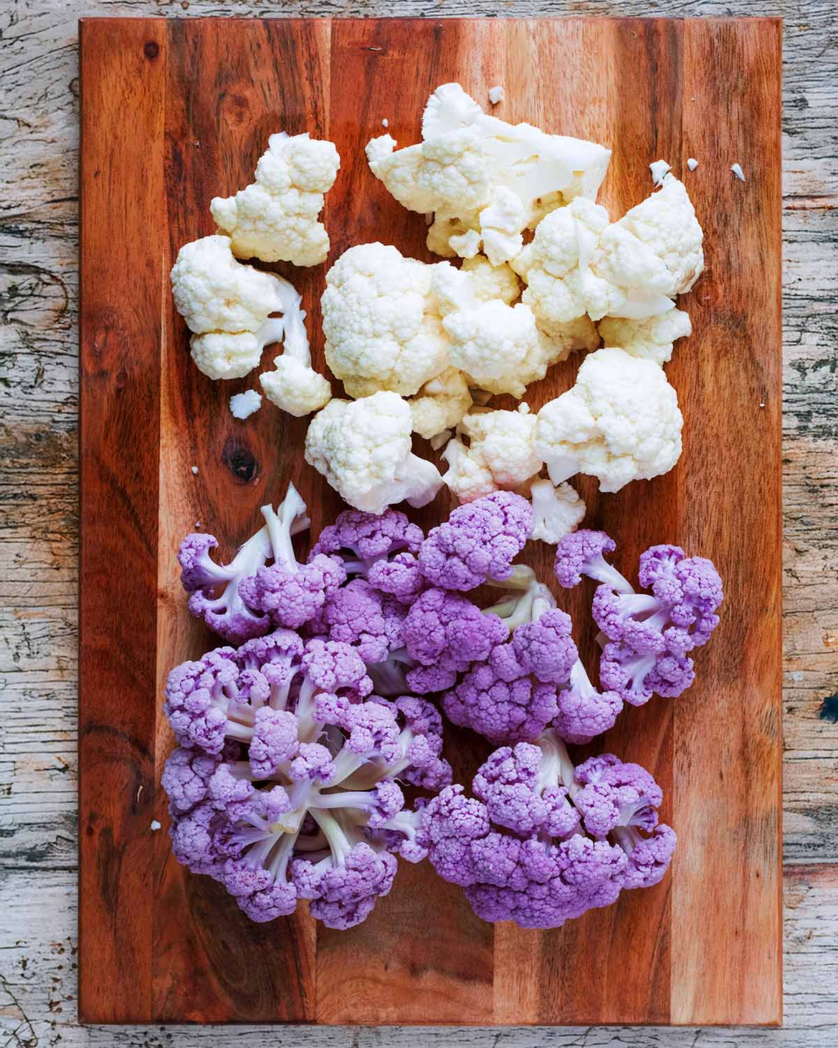 White and purple cauliflower florets on a wooden chopping board.