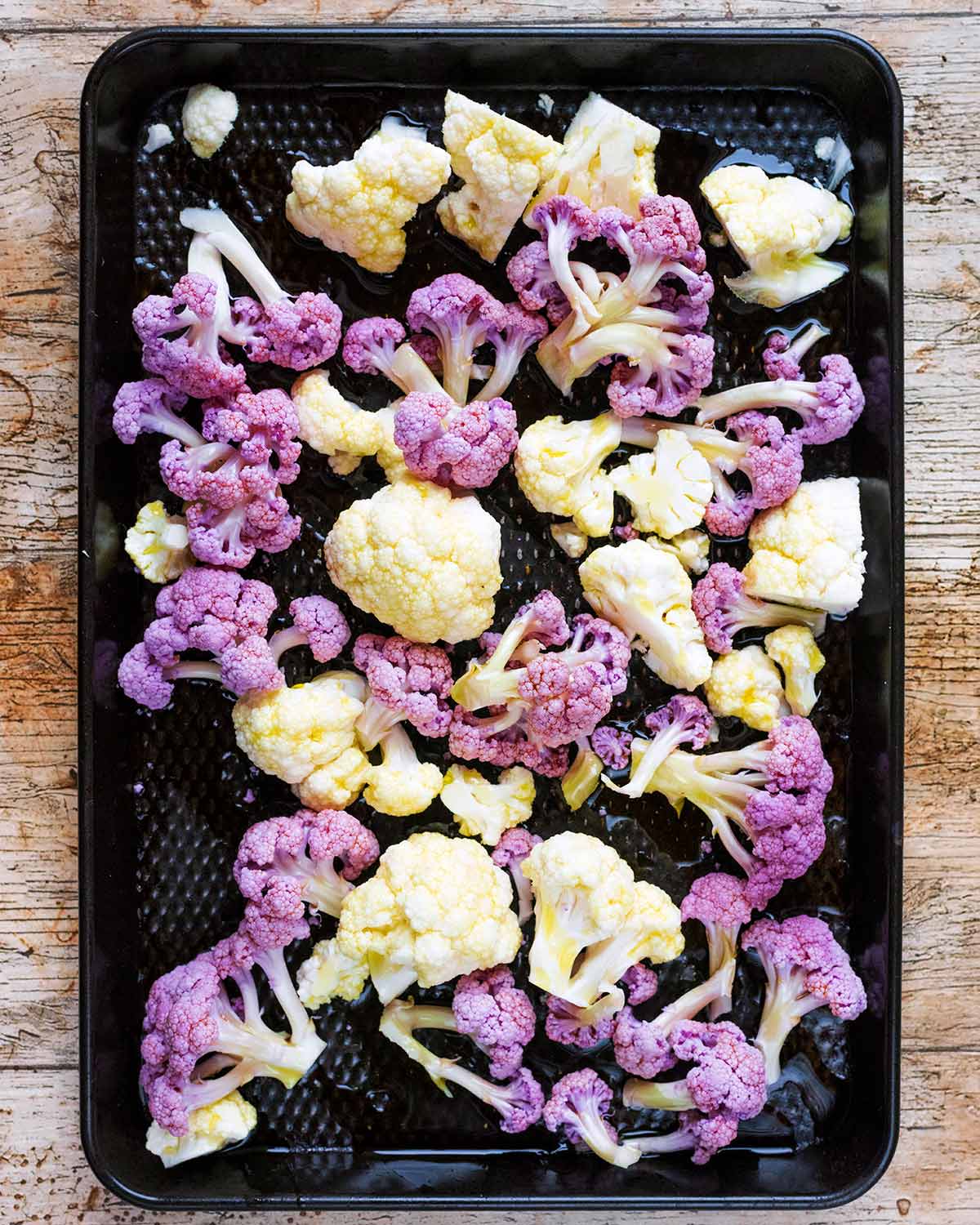 Cauliflower florets on a black baking tray.