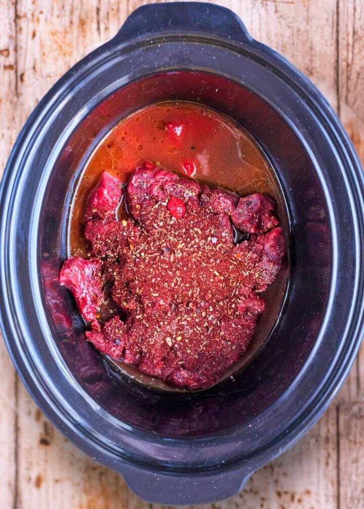 A slow cooker bowl containing beef, stock and spices.