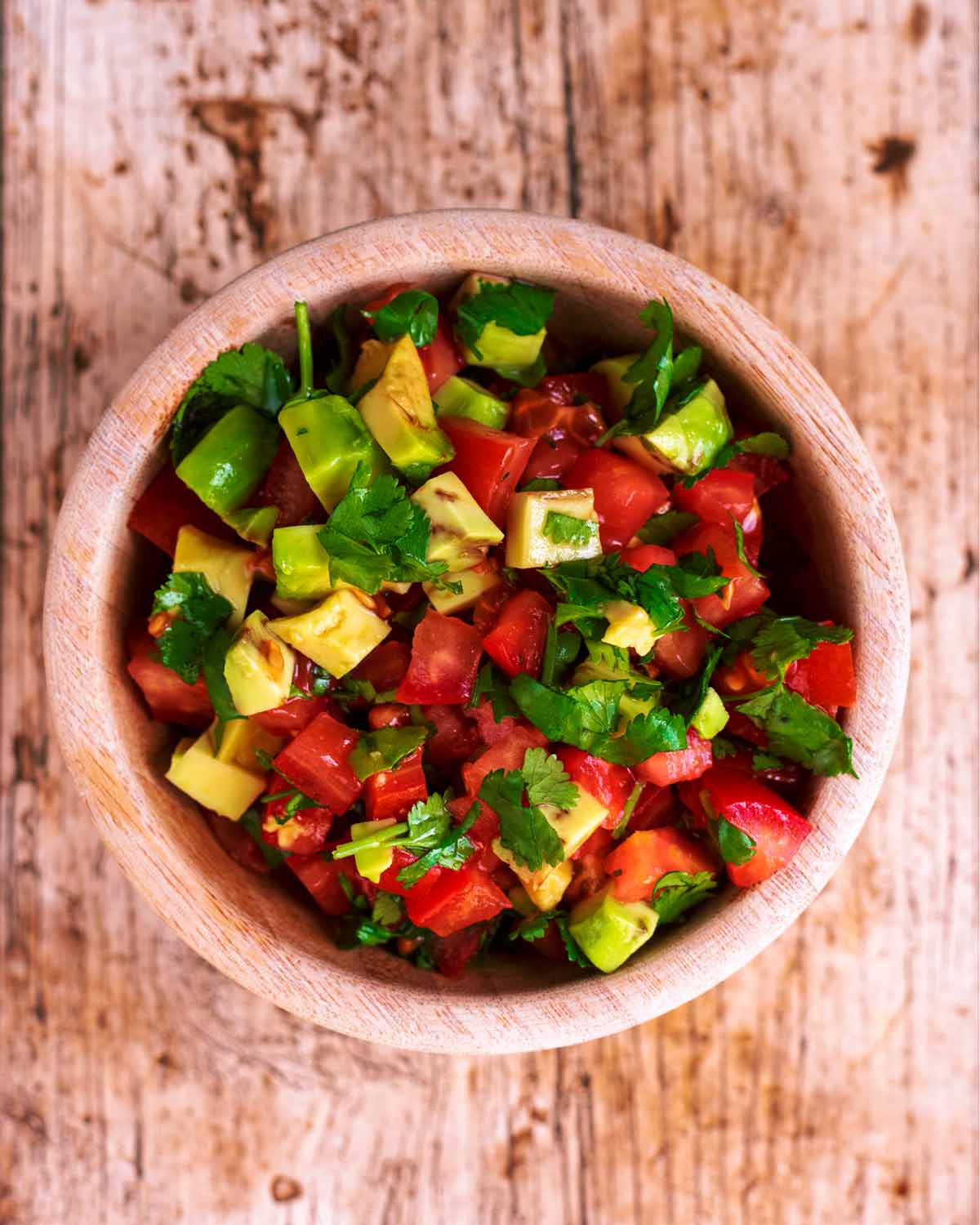 A small wooden bowl containing chopped tomato and avocado salsa