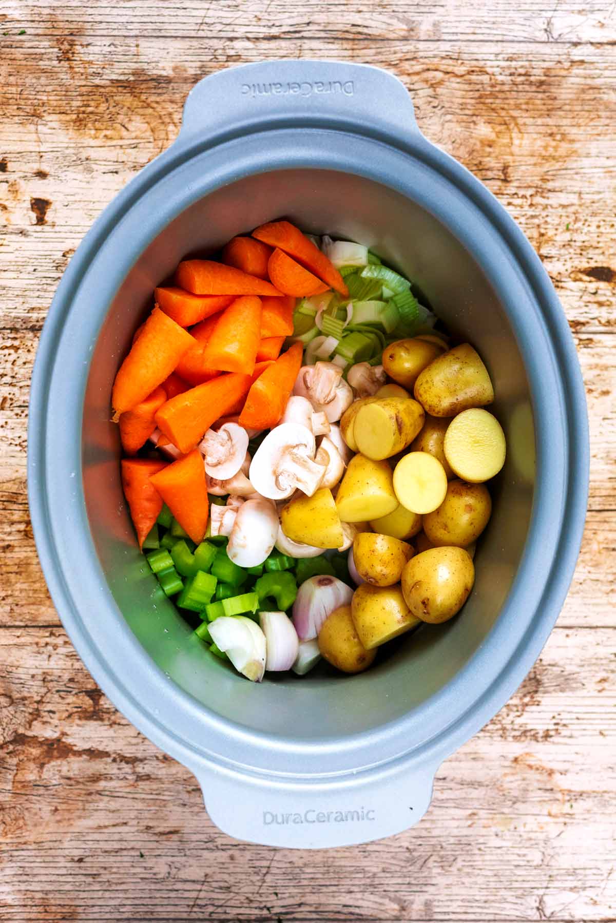 A slow cooker pot with chopped vegetables in it.