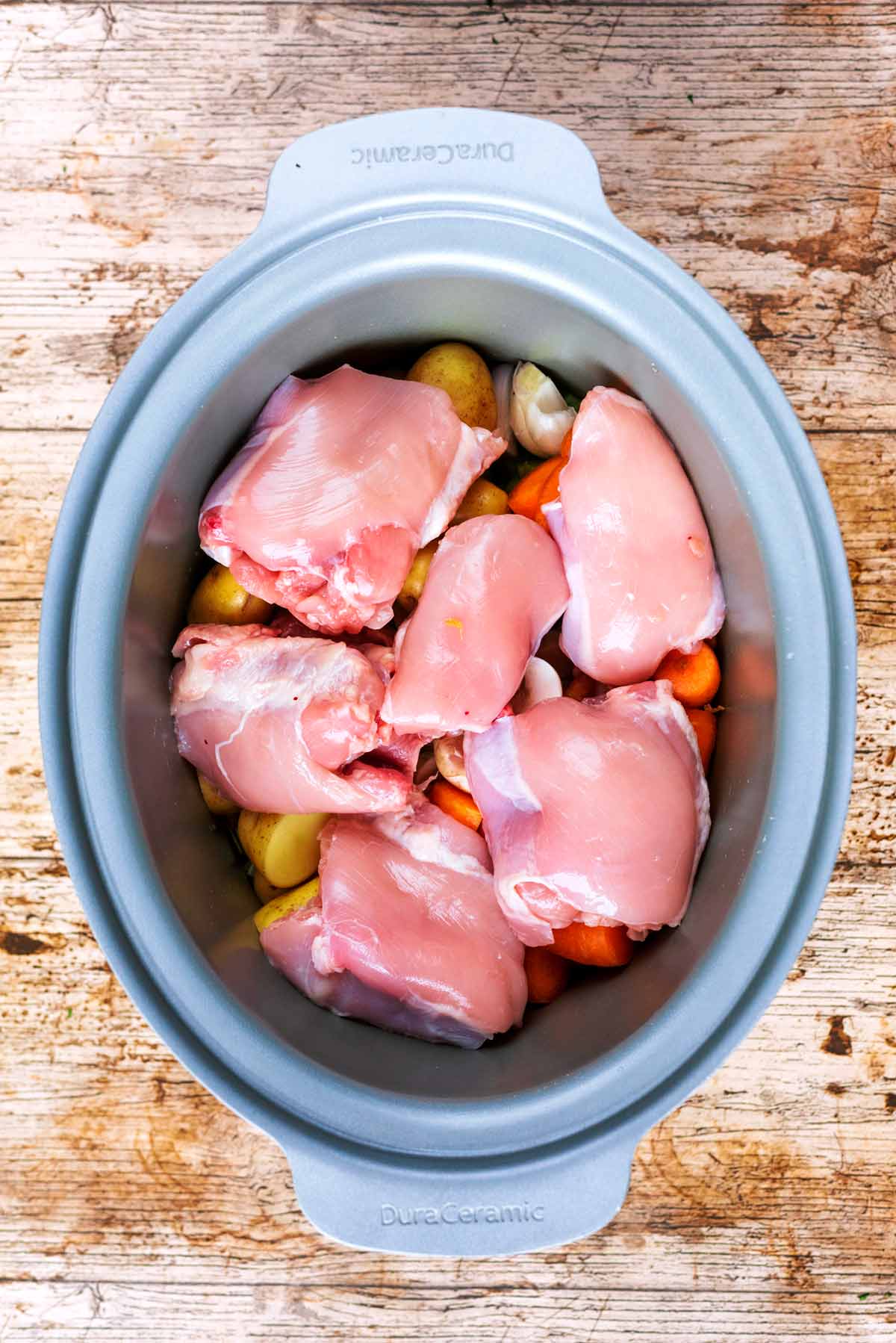 Chicken thighs and vegetables in a slow cooker pot.