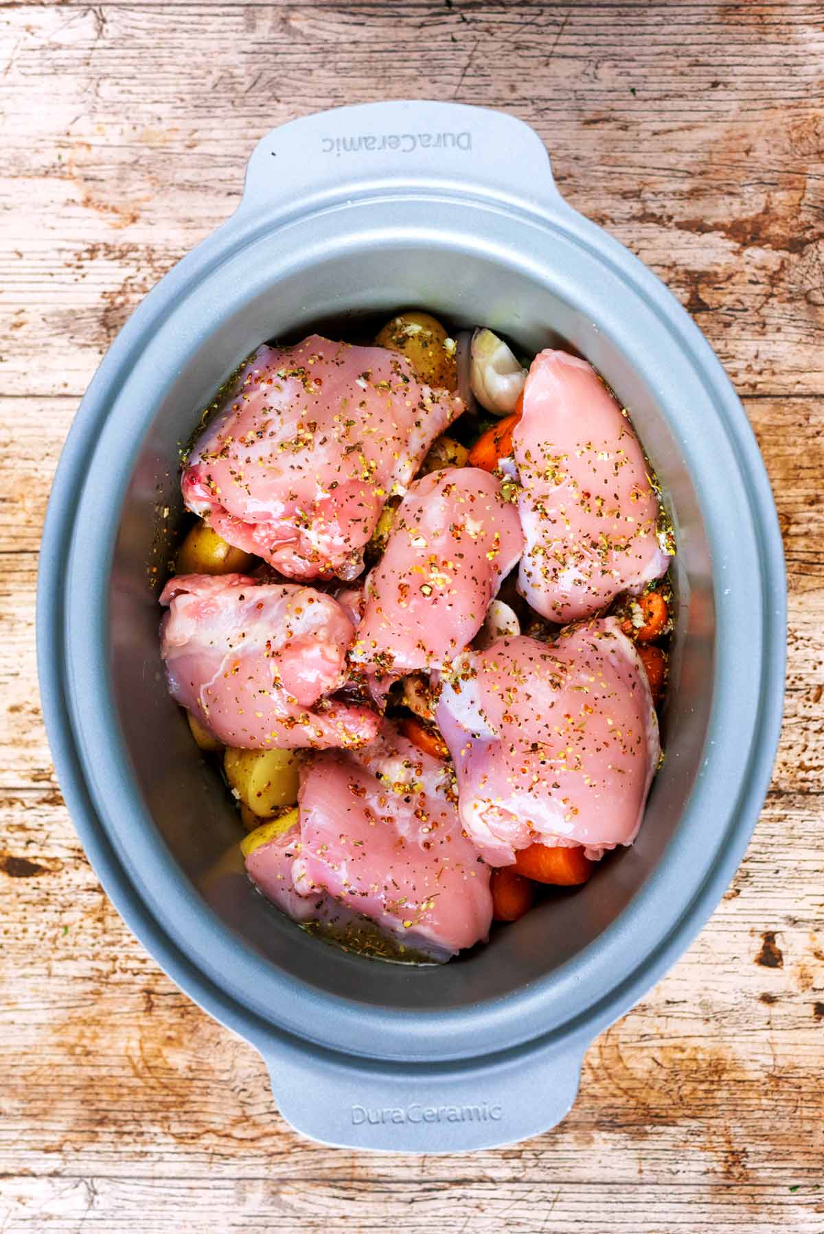 Chicken and vegetables in a slow cooker with stock and herbs.