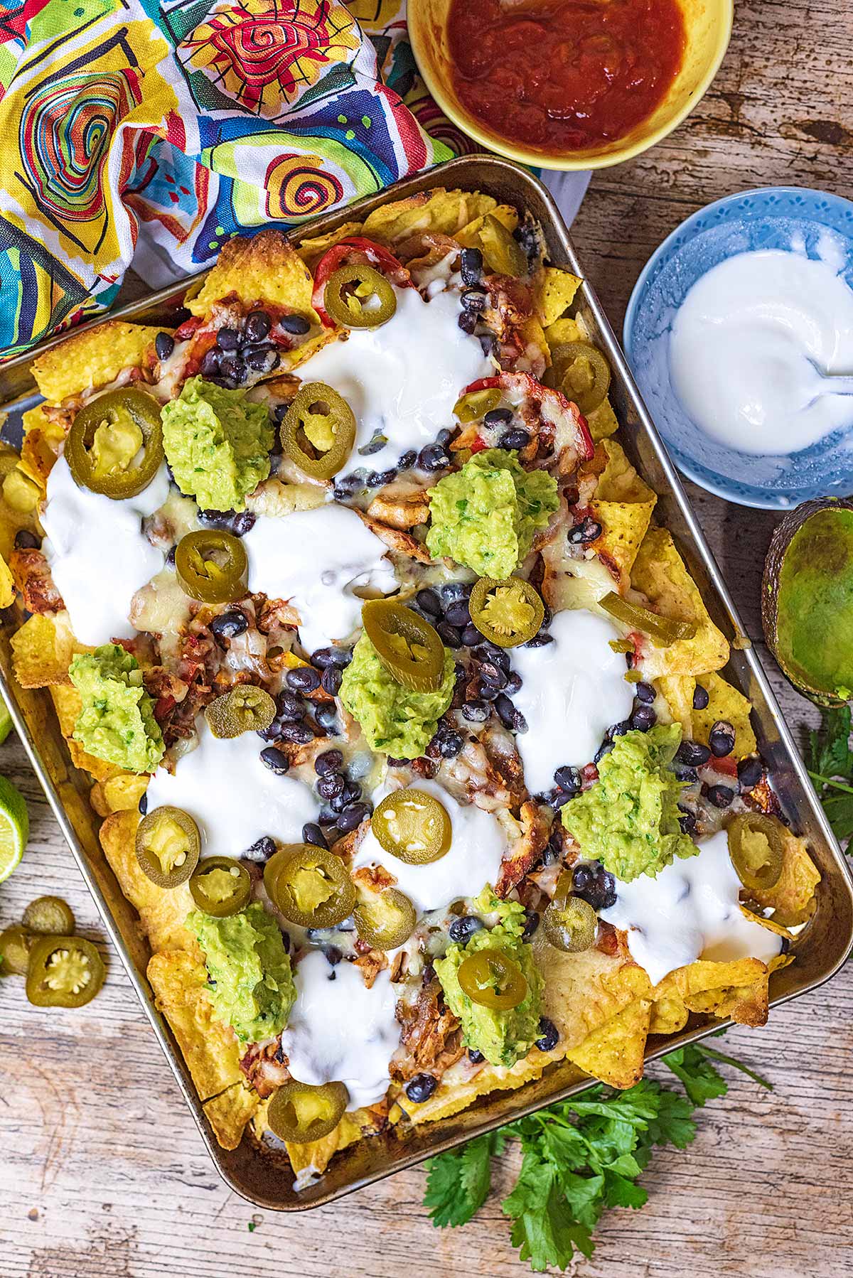 A large tray of nachos topped with sour cream, guacamole and salsa.