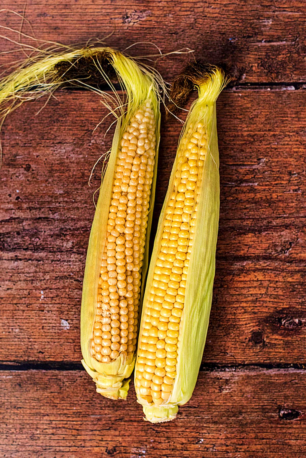 Two ears of corn on a wooden surface.