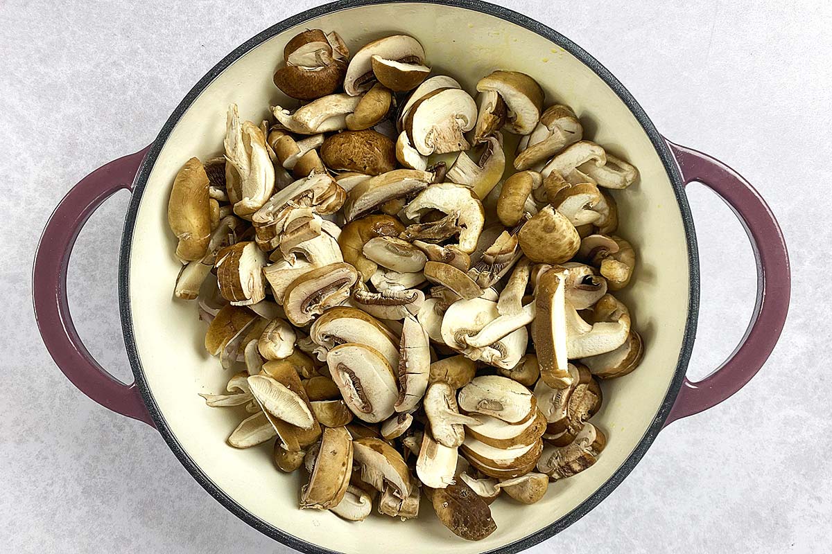 Sliced mushrooms cooking in a large pan.