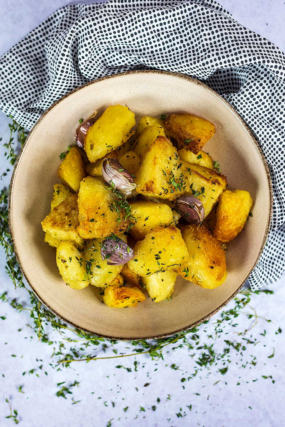 A bowl of crispy roast potatoes with three garlic cloves.