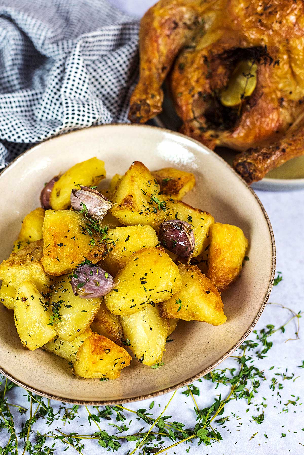 A bowl of roast potatoes in front of a whole roast chicken.