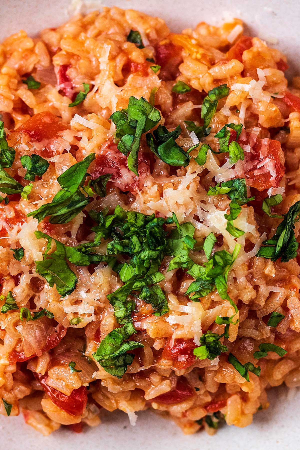 Tomato risotto with grated cheese and chopped herbs on top.