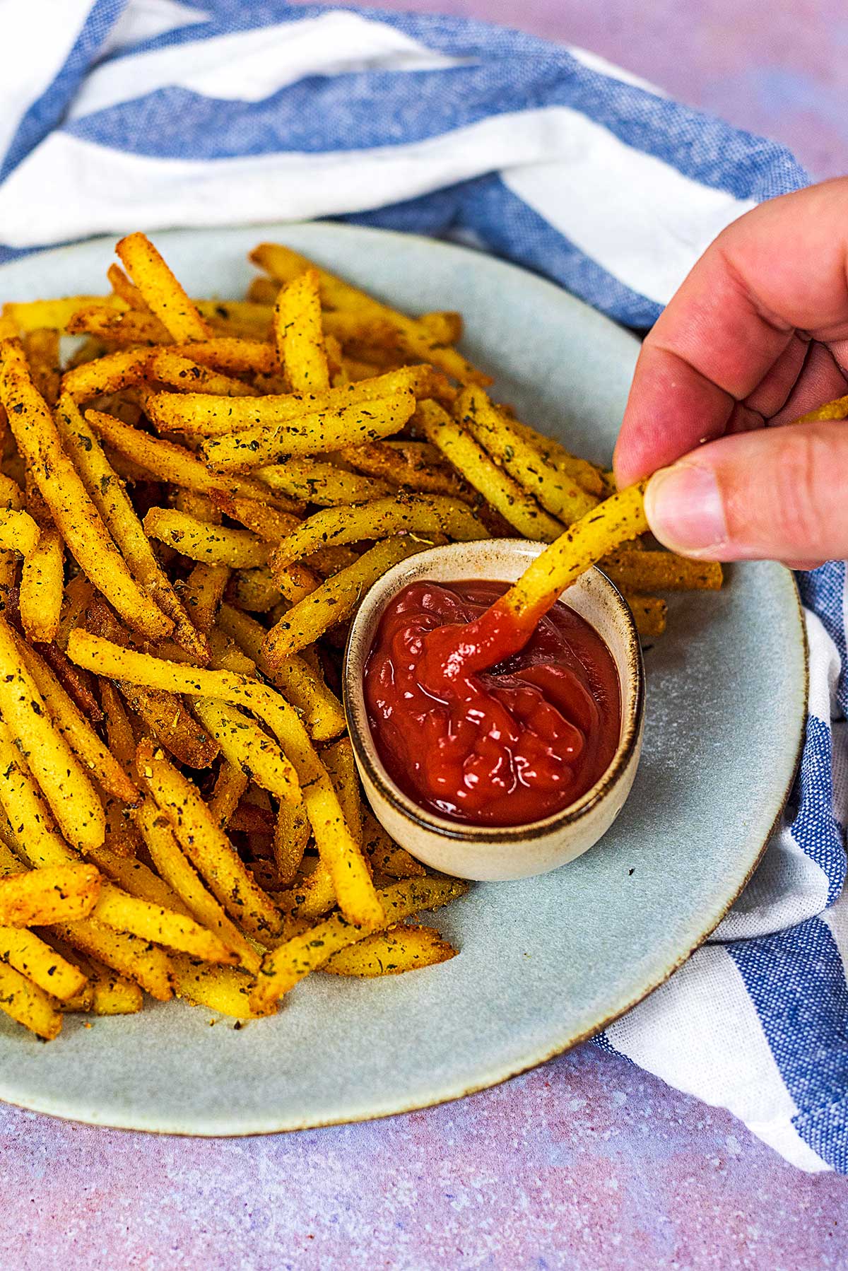A hand dipping a French fry into some ketchup.