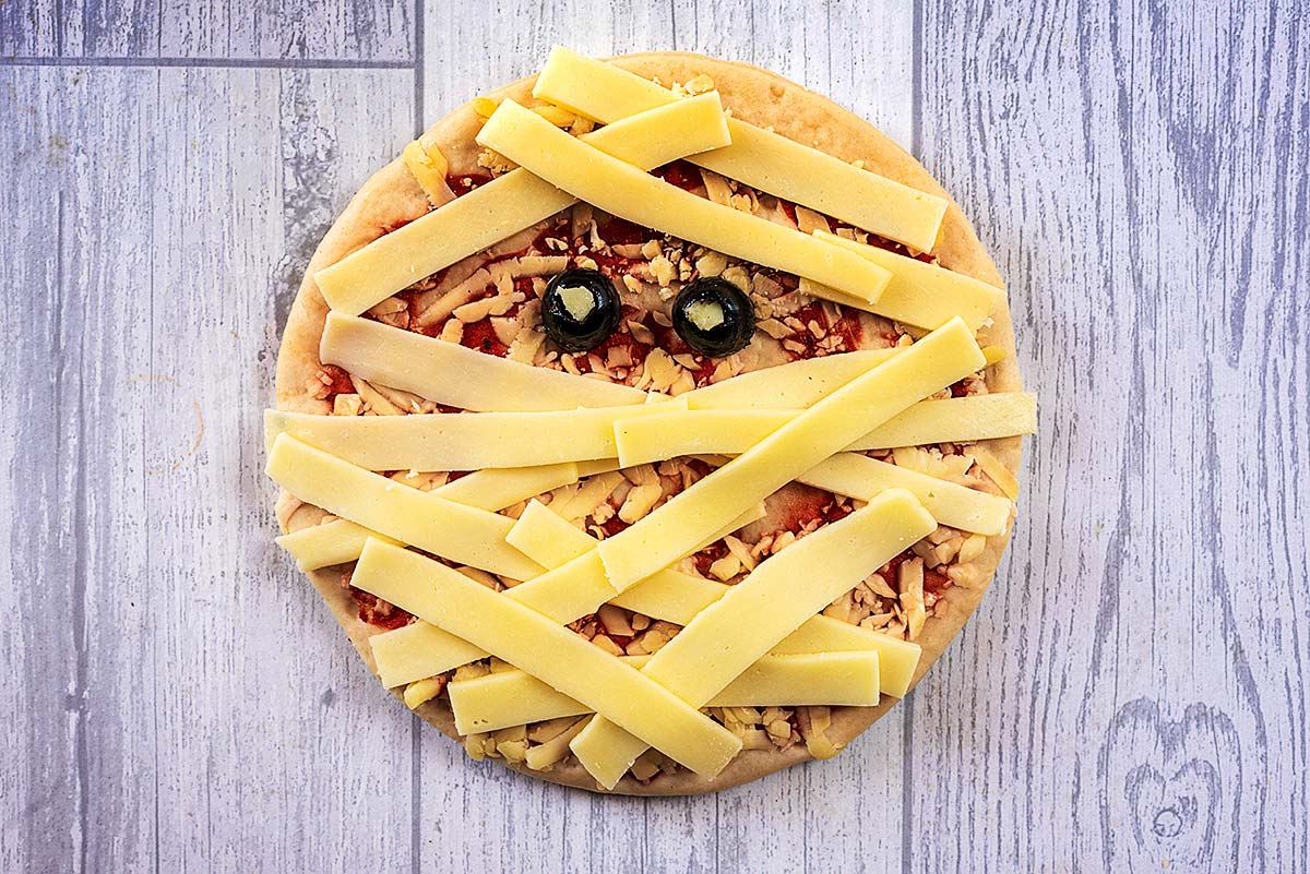 A pizza with strips of cheese across it and two olive halves, making it look like a mummy.