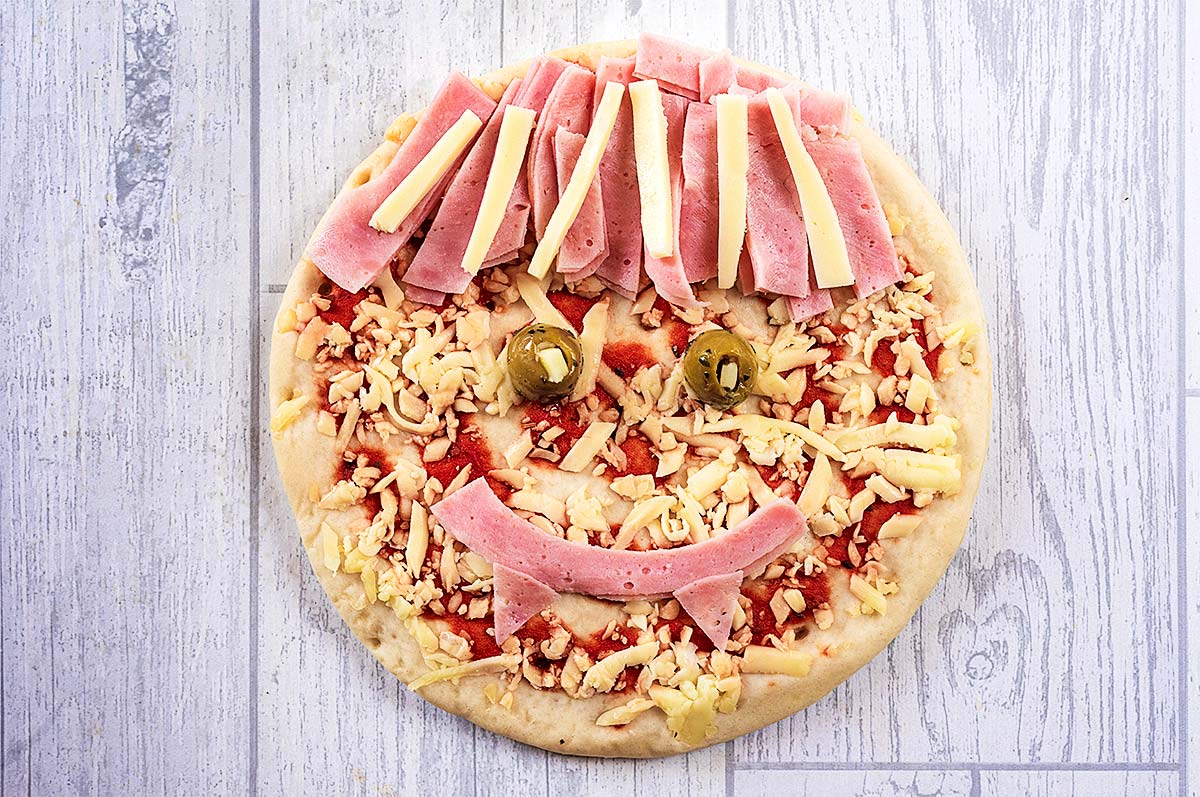 A pizza with strips of ham and cheese making it look like a vampire.
