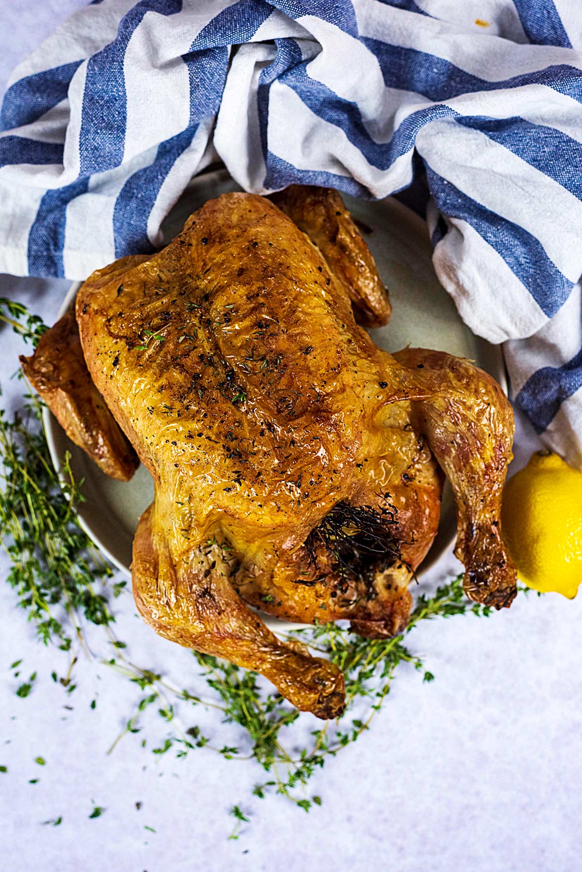 A whole roasted chicken on a plate next to a striped towel.