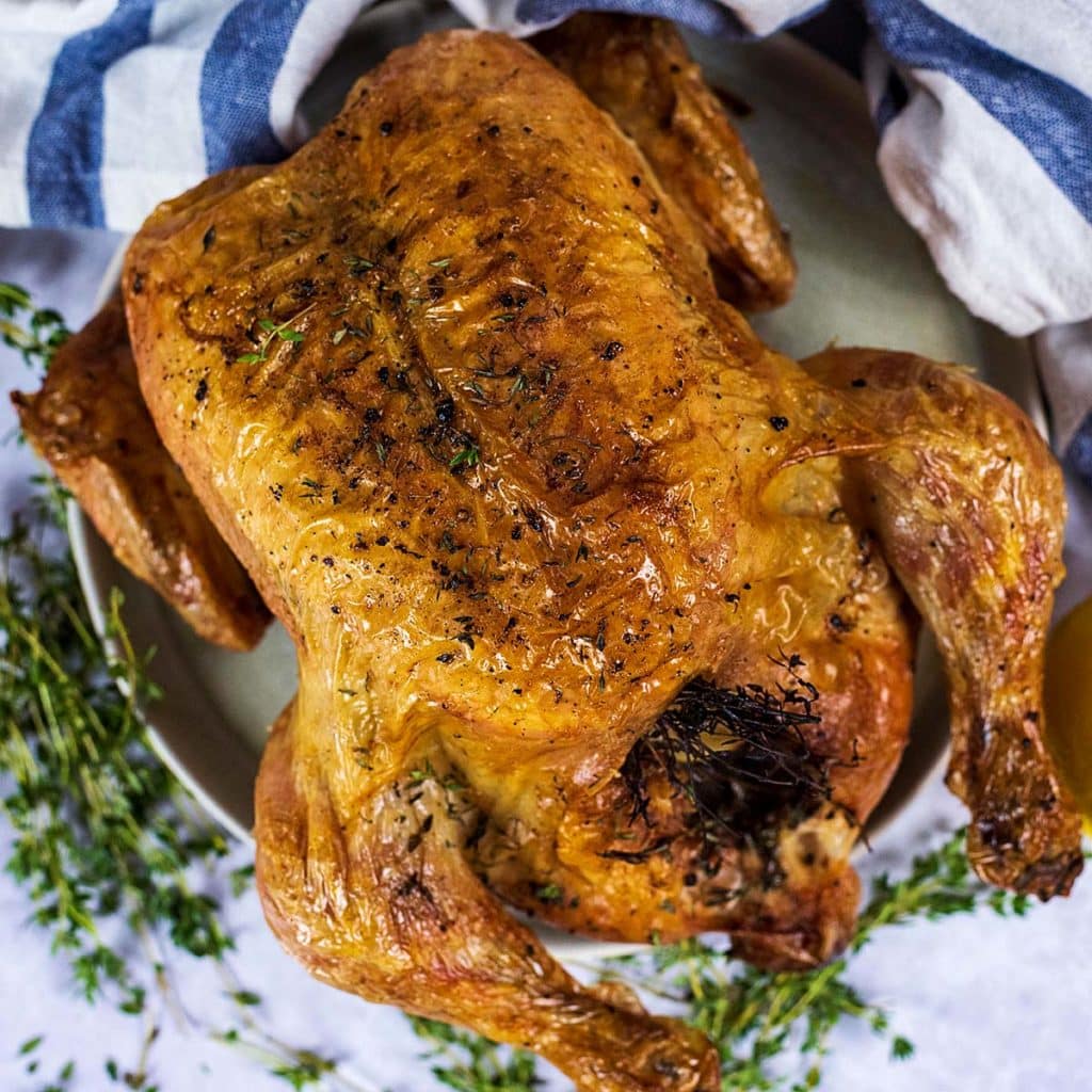 Perfect roast chicekn on a plate surrounded by sprigs of thyme.