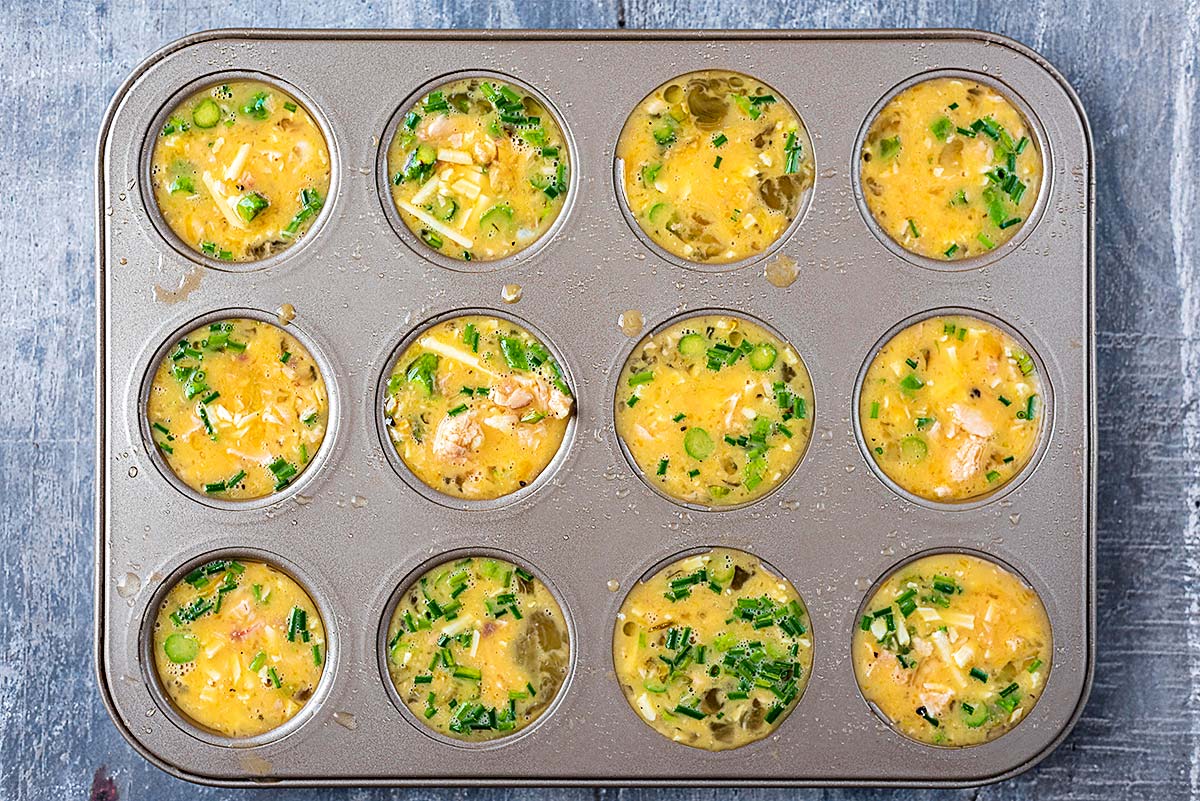 A twelve hole muffin tin containing an egg and salmon mixture.