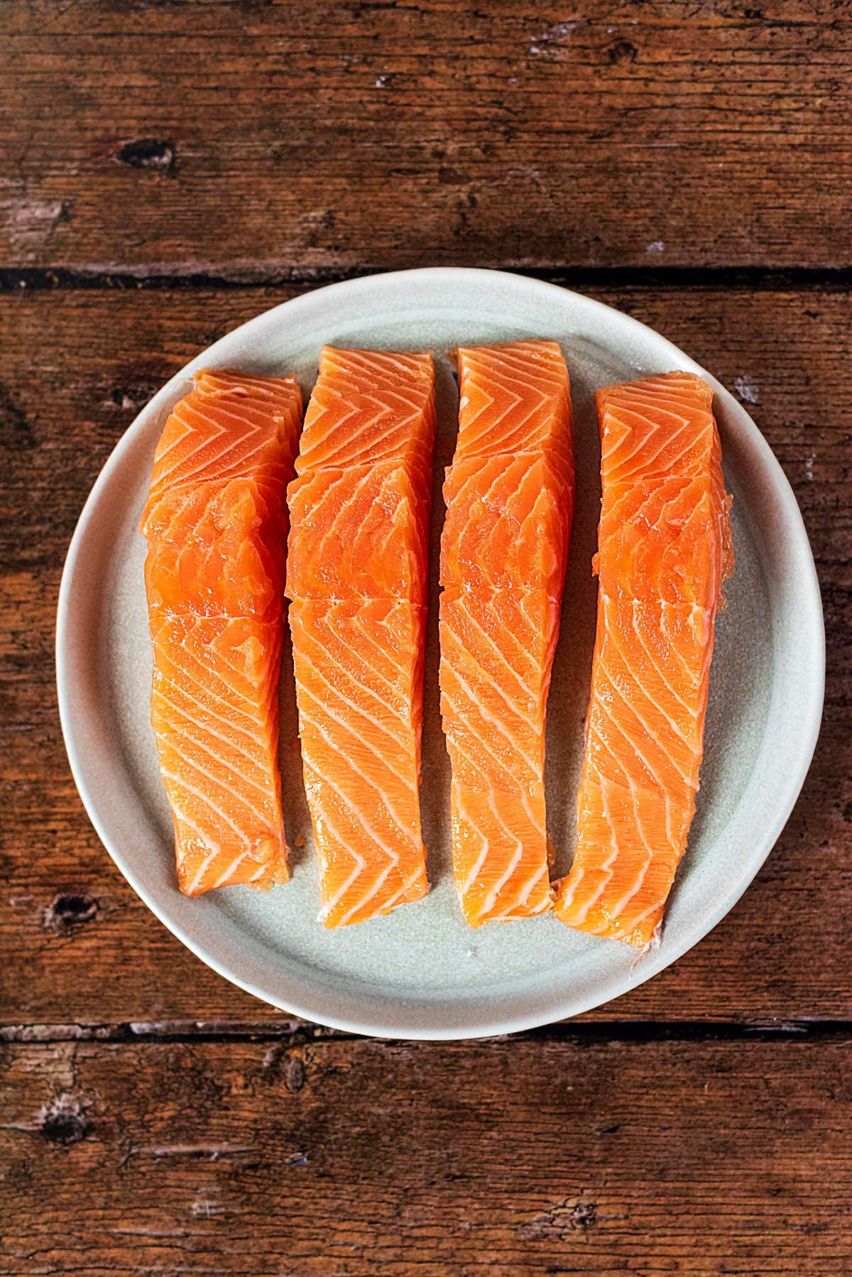 Four salmon fillets on a round plate.