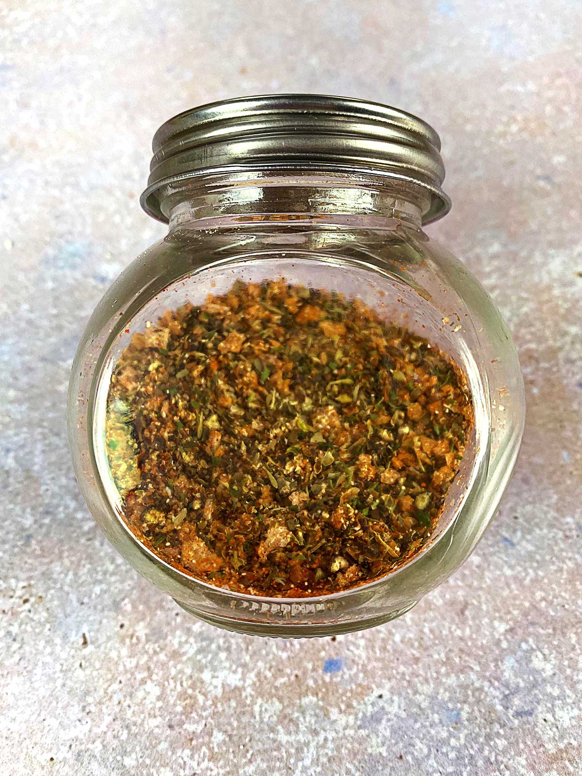 A glass jar full of mixed herbs and spices.