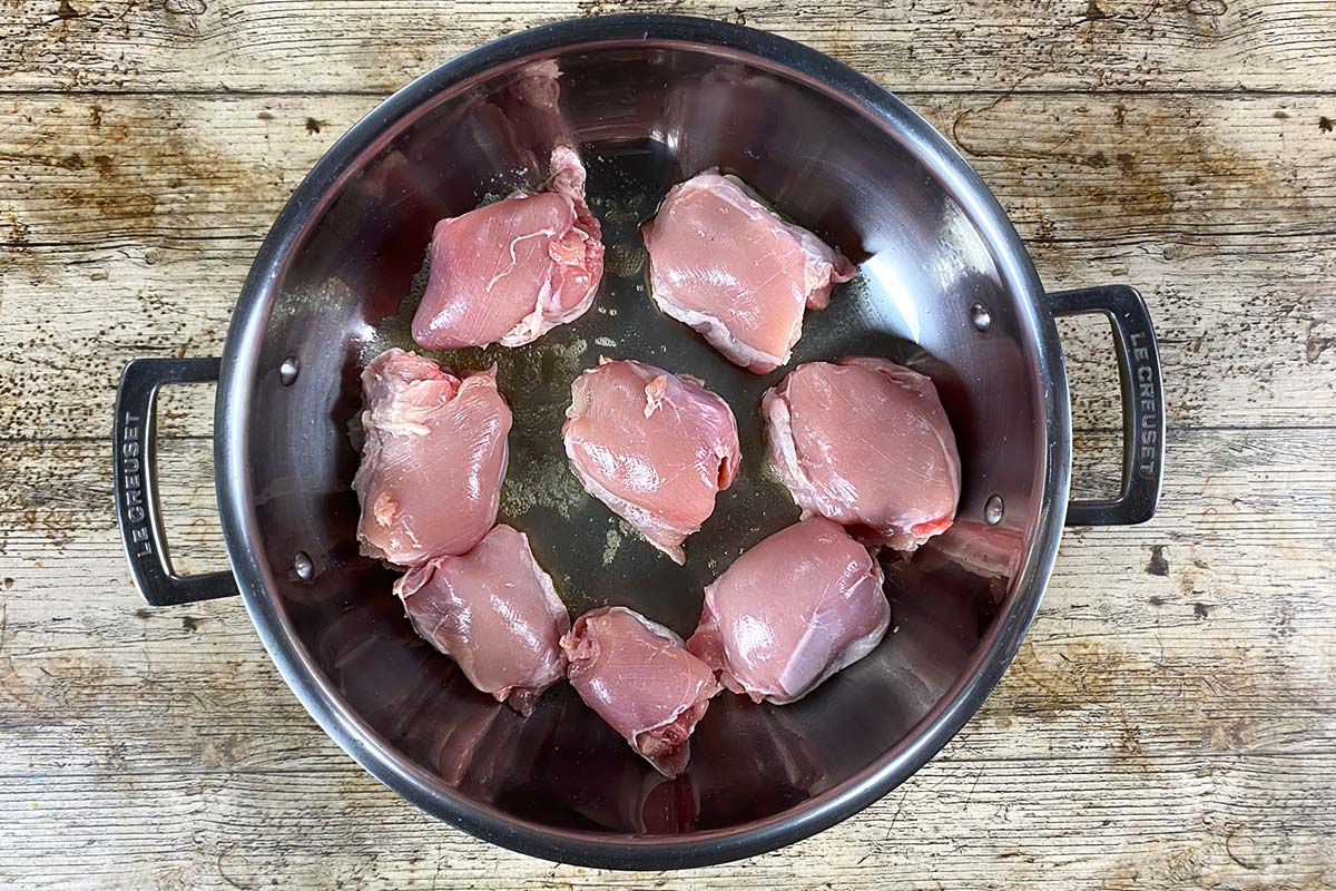 Eight chicken thighs browning in a large silver pan.