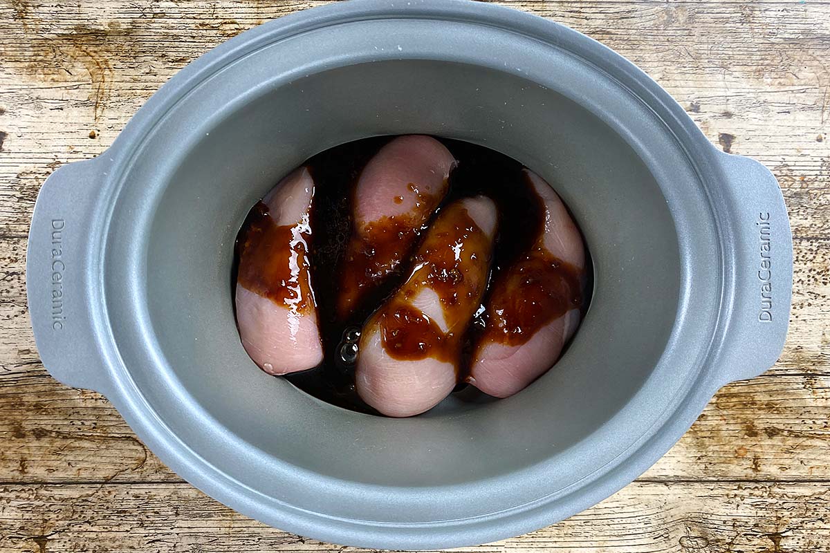A slow cooker bowl with four chicken breasts and teriyaki sauce.