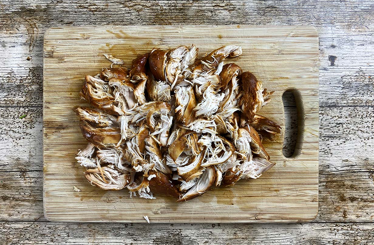 A wooden chopping board with chopped teriyaki chicken on it.