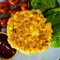 Sweetcorn fritters on a plate with dip, tomatoes and salad.