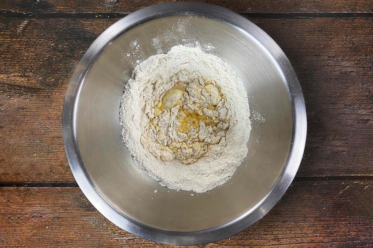 A metal mixing bowl with flour and beaten eggs in it.