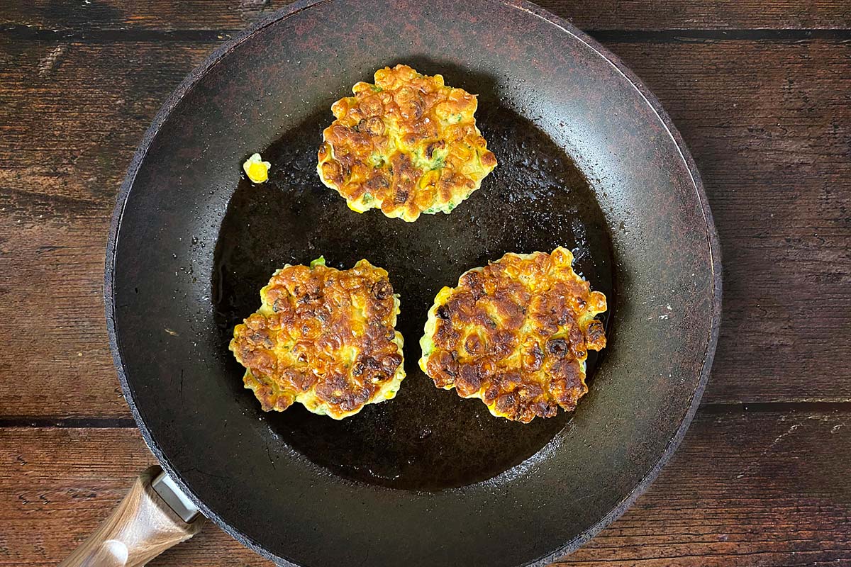 Sweetcorn fritters cooking in a frying pan.