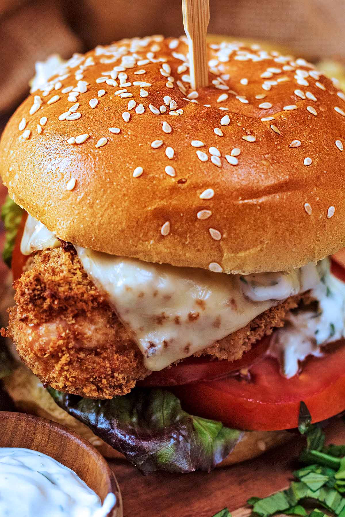 Breaded chicken topped with cheese in a sesame seed brioche bun with lettuce and tomato.