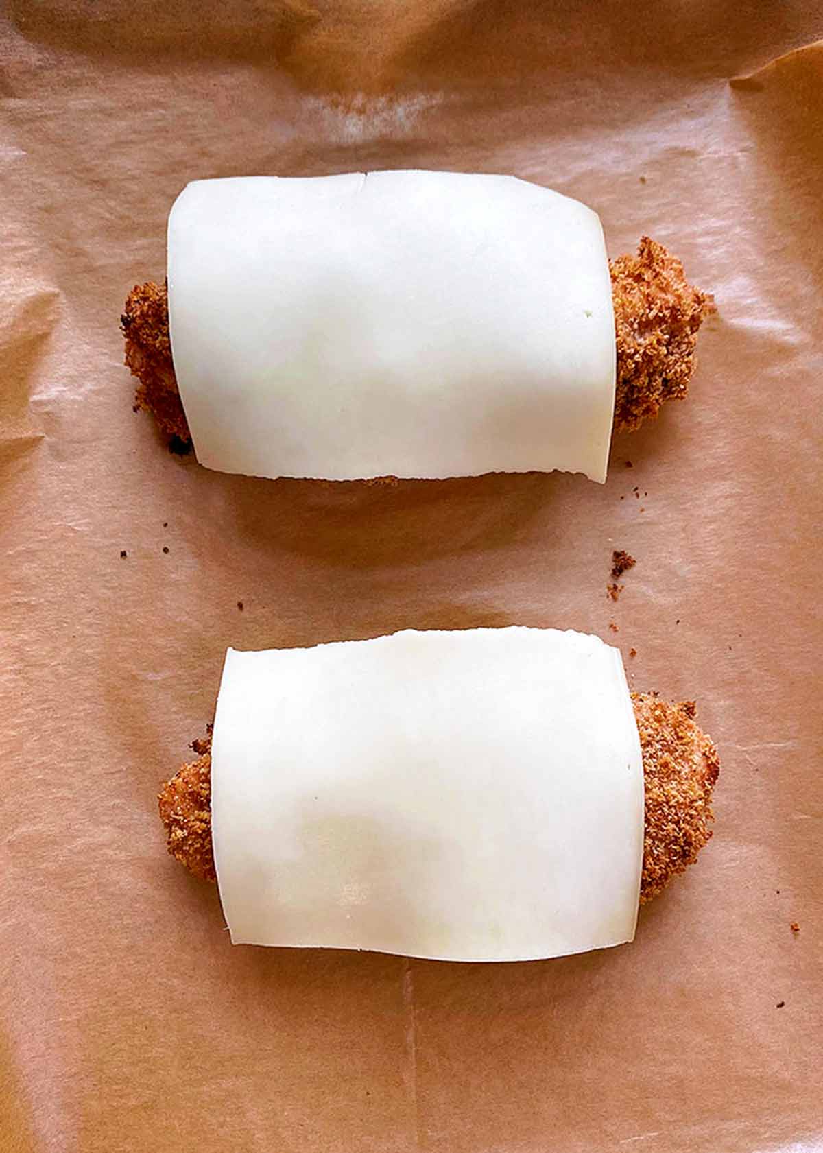 Two breaded chicken breasts with cheese slices on them.