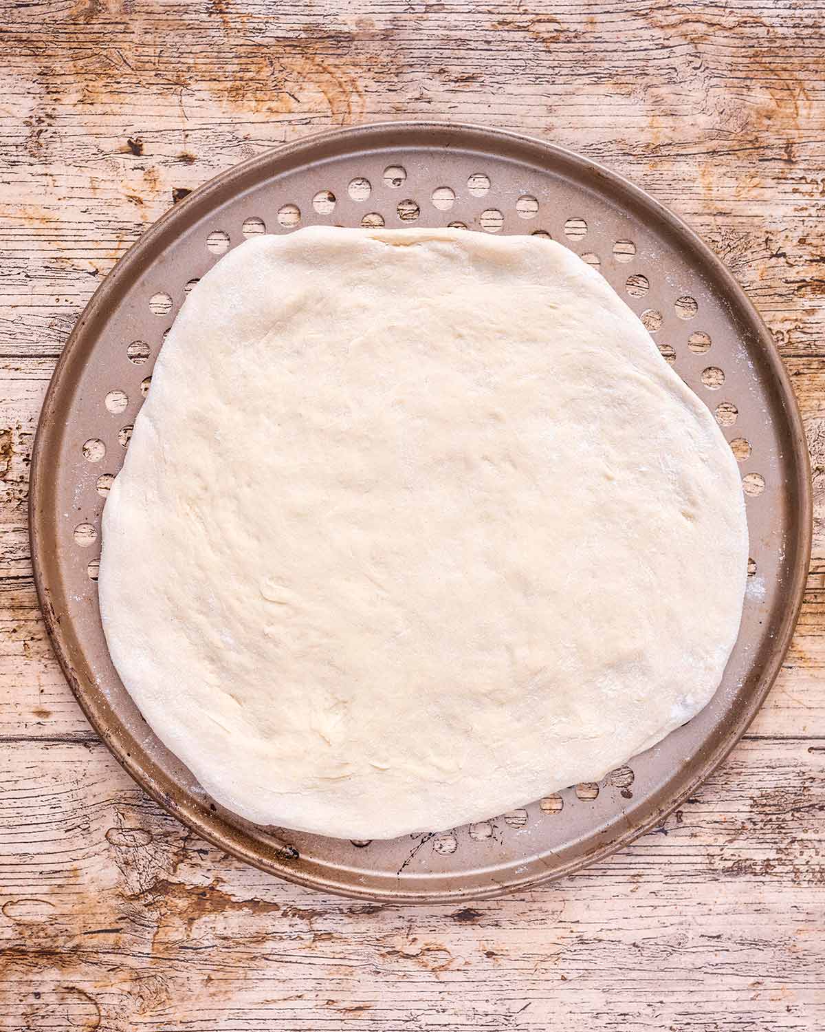 Pizza dough stretched out on a pizza cooking tray.