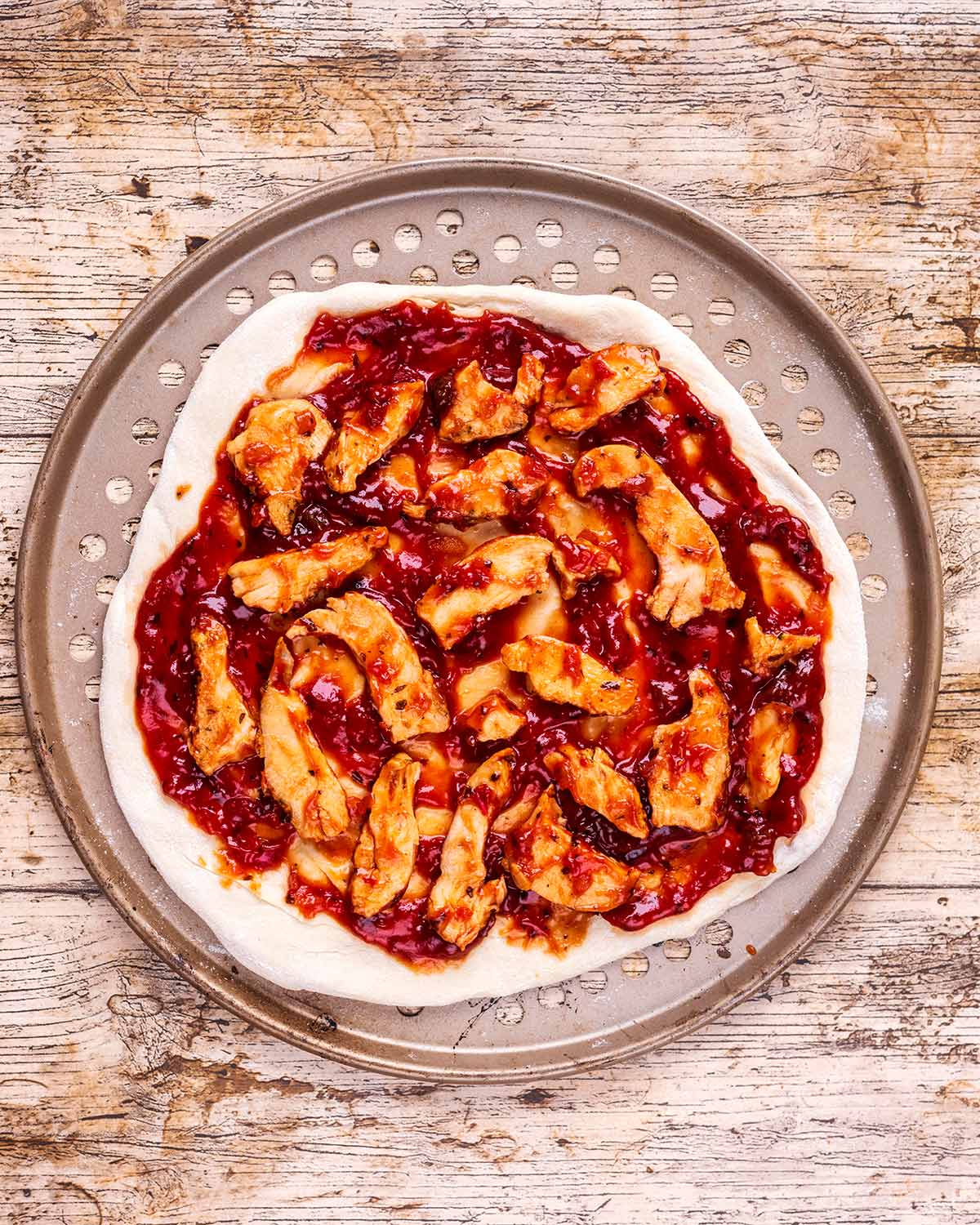 Pizza dough covered by barbecue sauce and pieces of chicken.