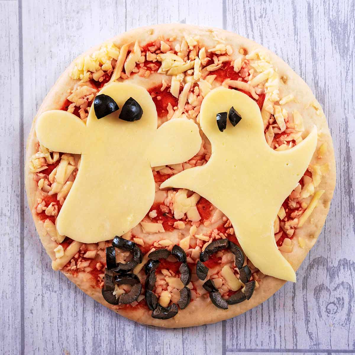 A pizza with two ghosts cut out of cheese on top.