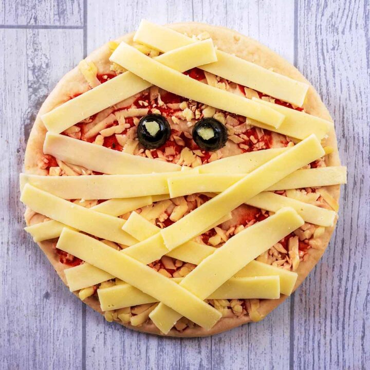A pizza with strips of cheese across it and two olive halves, making it look like a mummy.