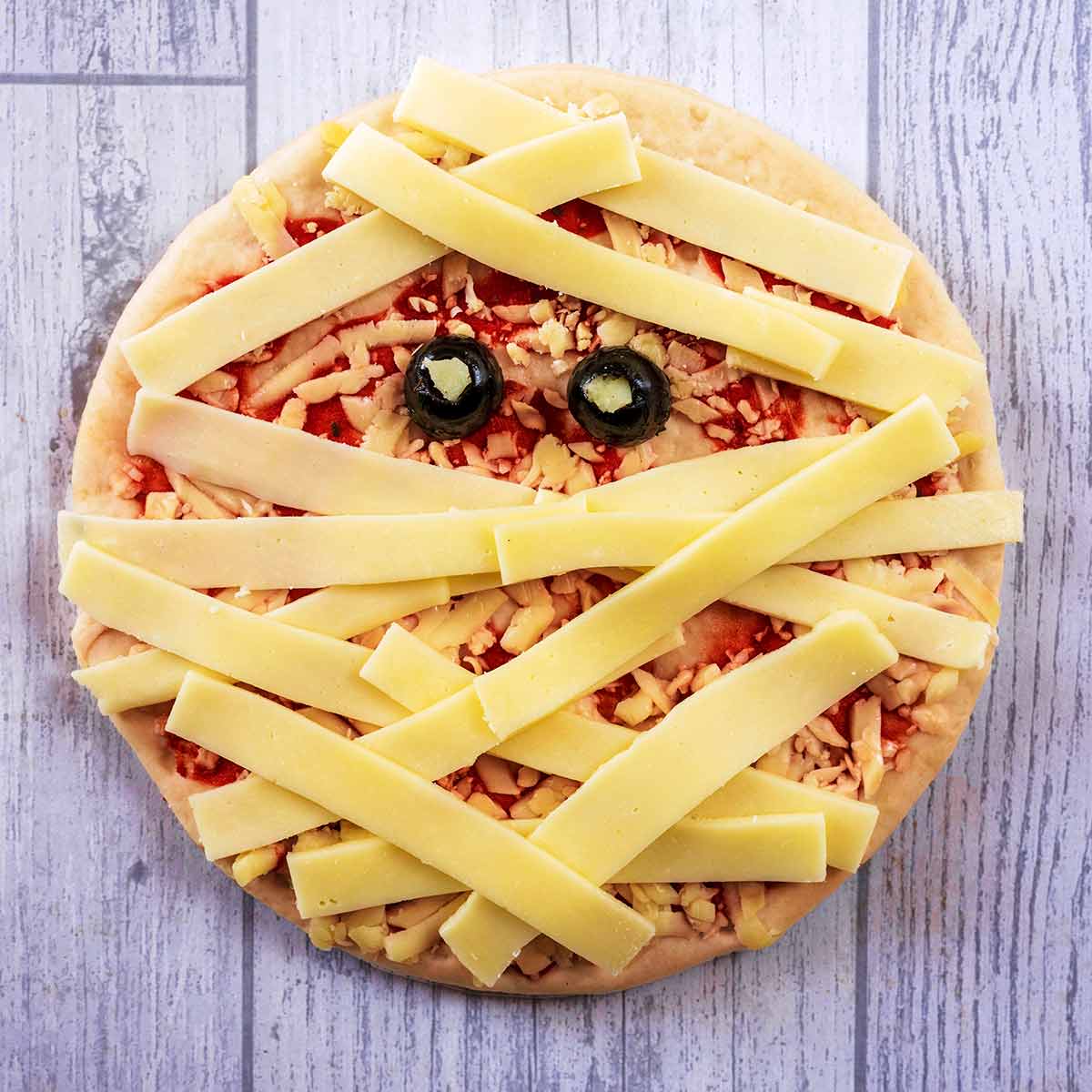 A pizza with strips of cheese across it and two olive halves, making it look like a mummy.