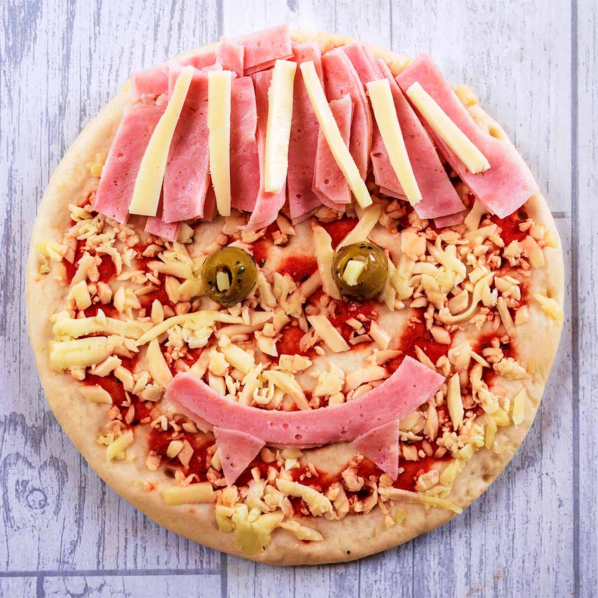 A pizza with strips of ham and cheese making it look like a vampire.