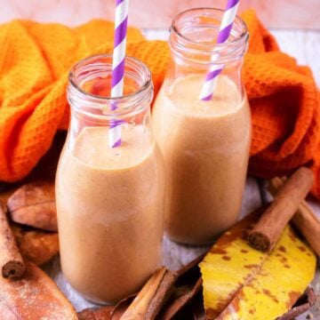 Two glass bottles full of pumpkin smoothie with leaves scattered around them.