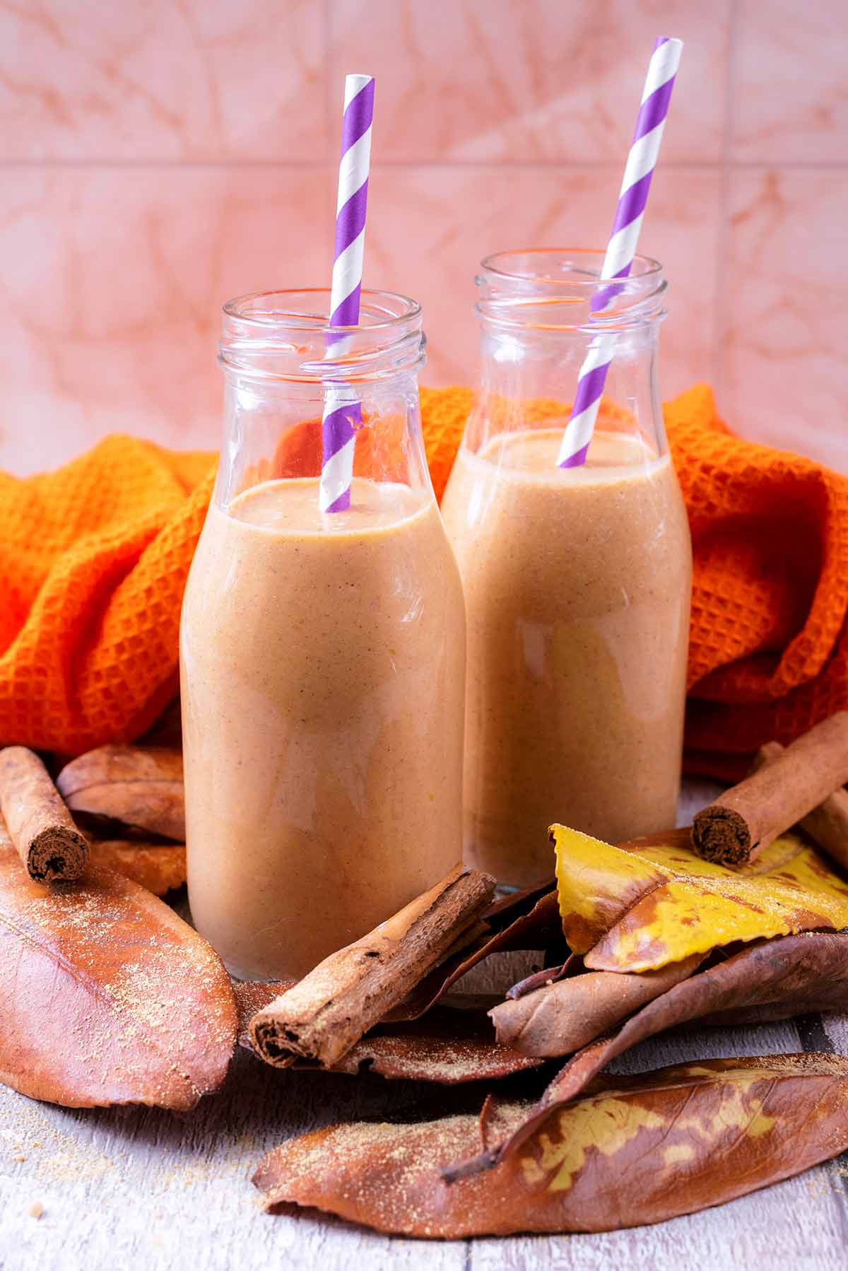 Two small milk bottles containing pumpkin smoothie with striped straws.