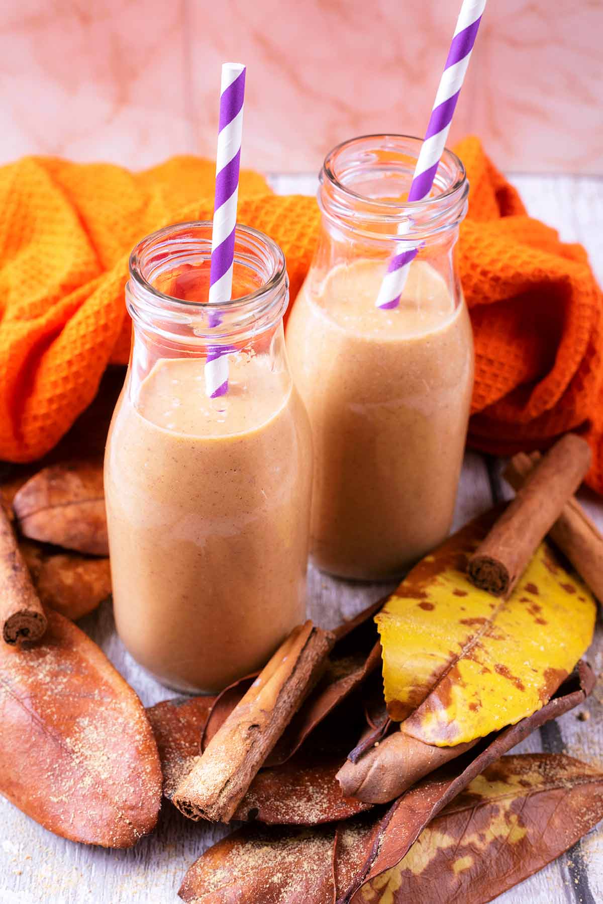 Pumpkin smoothie in two glass bottles surrounded by brown leaves.
