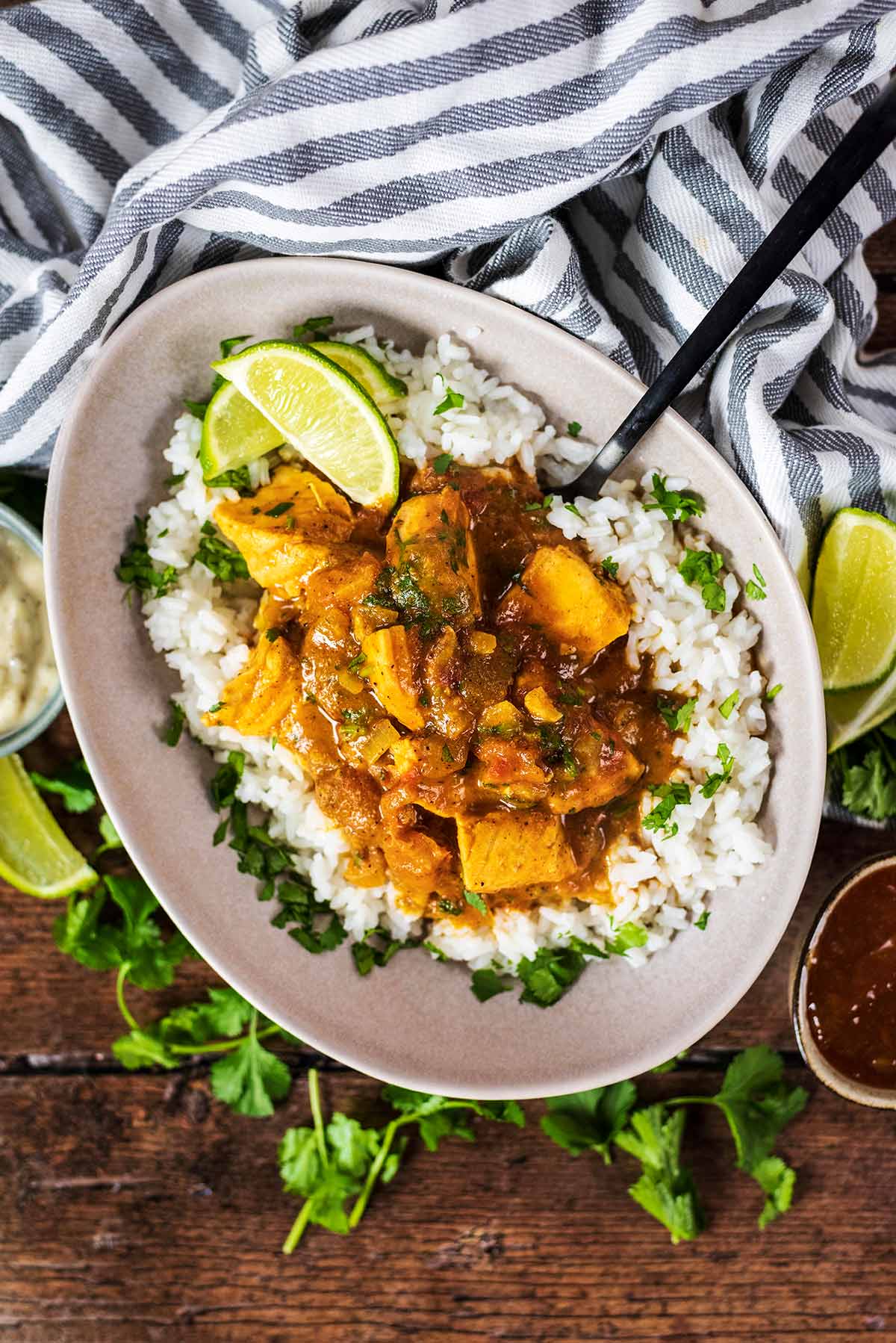 A bowl of curry on a bed of rice next to a striped towel and small pots of sauce.