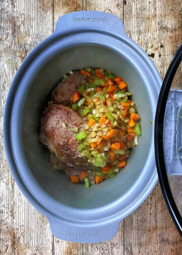 Seared beef and cooked vegetables in a slow cooker pot.