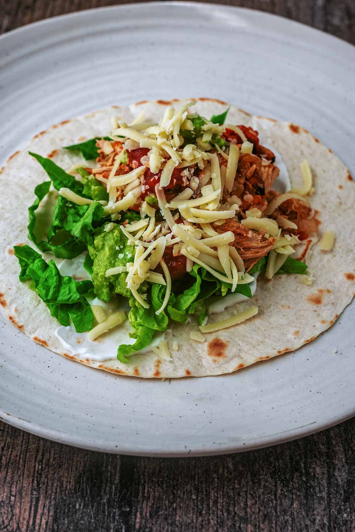 A tortilla wrap topped with sour cream, lettuce, fajita mixture and grated cheese.