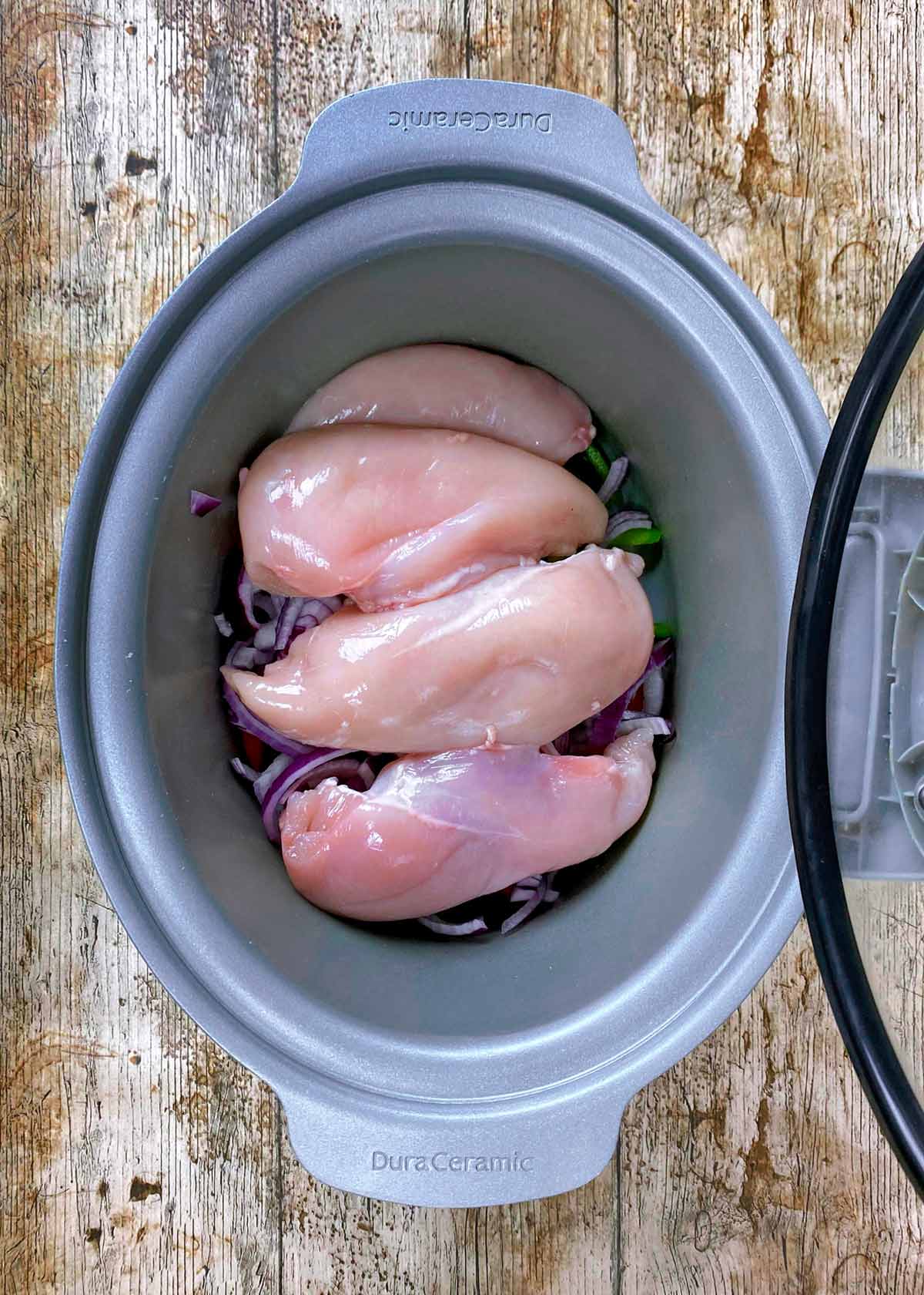 Whole chicken breasts on top of sliced vegetables in a slow cooker.