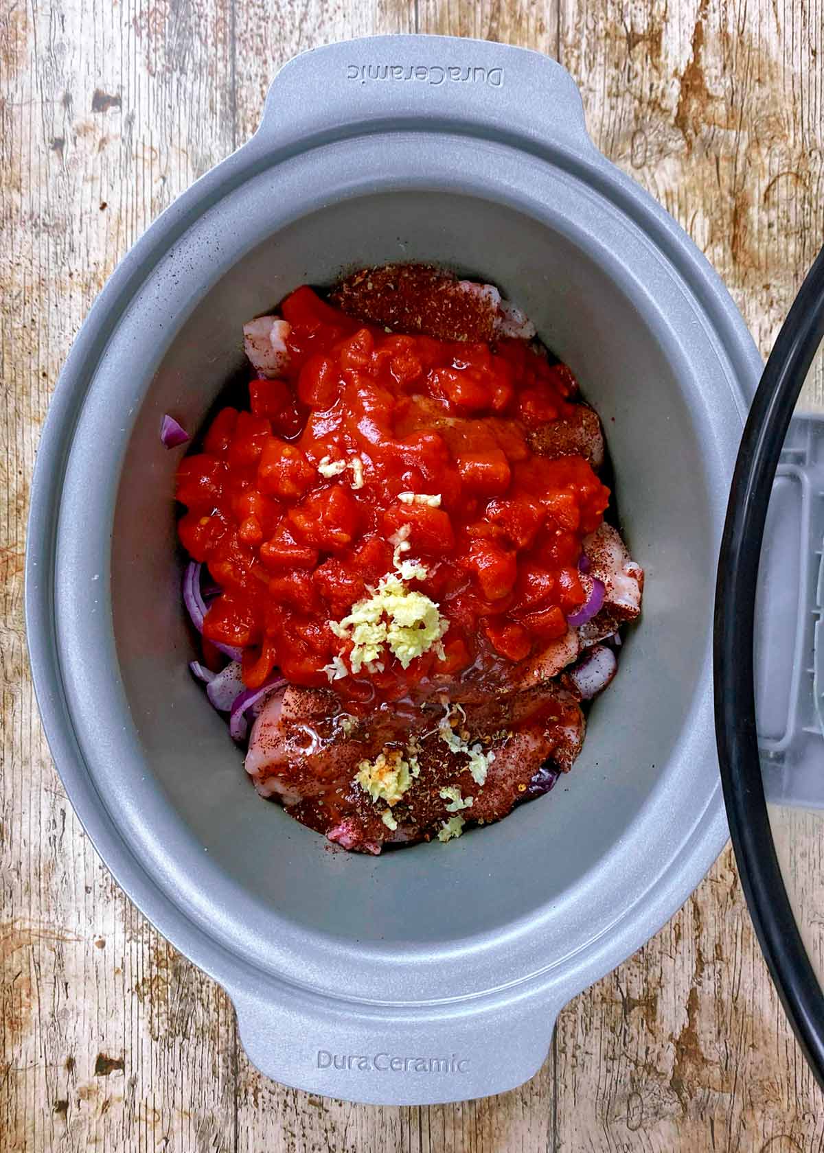 Chopped tomatoes and crushed garlic covering chicken and veg in a slow cooker.