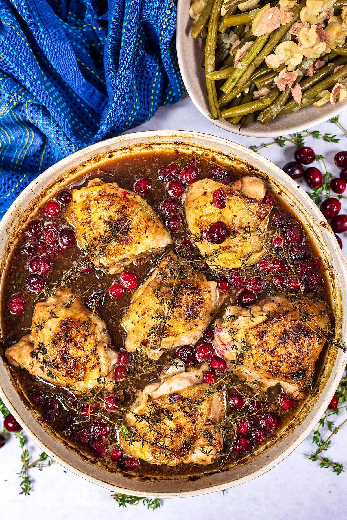 A large round dish containing cooked chicken thighs in a cranberry gravy.