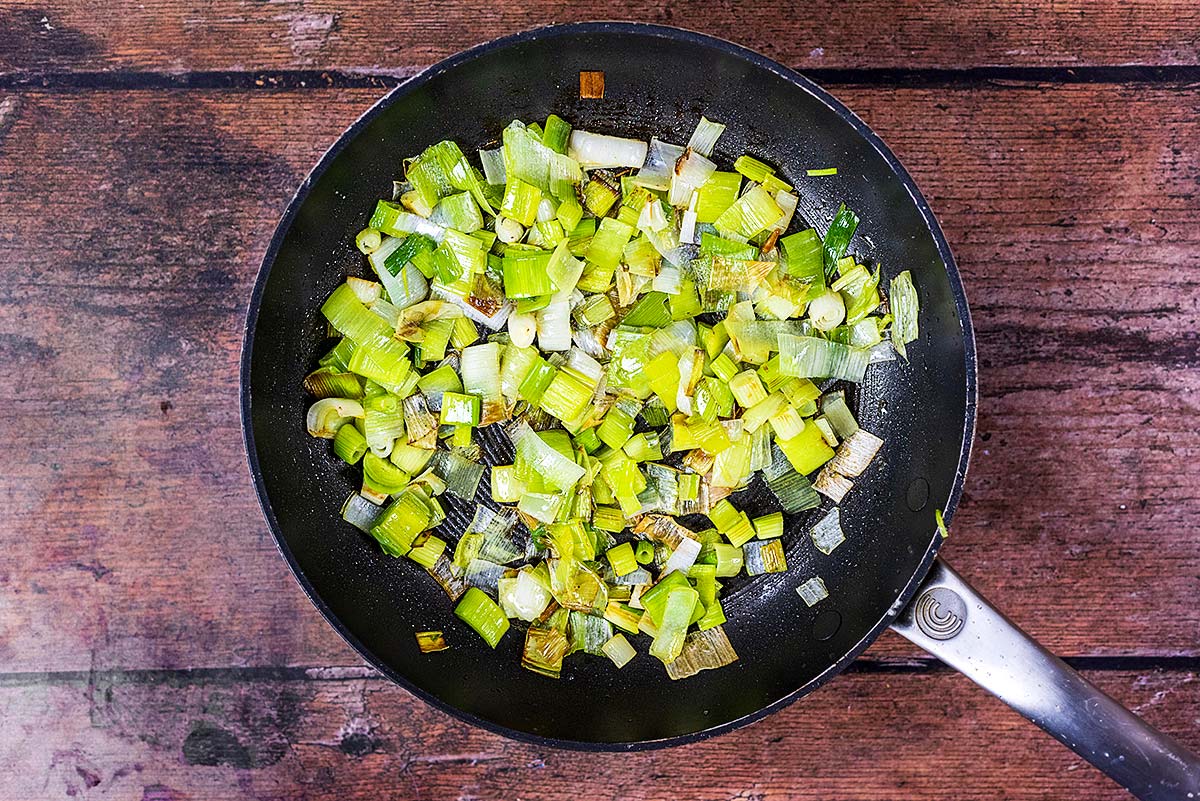 Chopped leeks and scallions cooking in a frying pan.