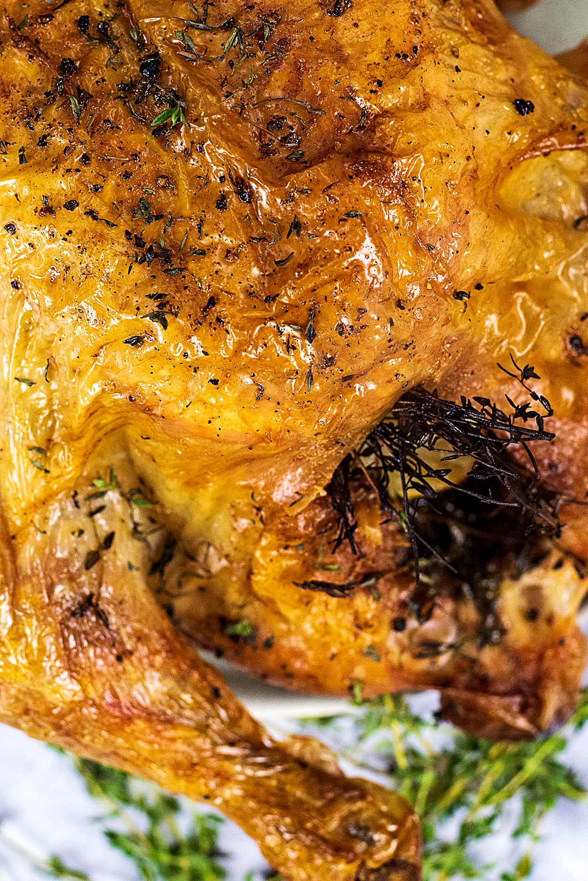 A roast chicken showing the cavity with sprigs of thyme poking out.