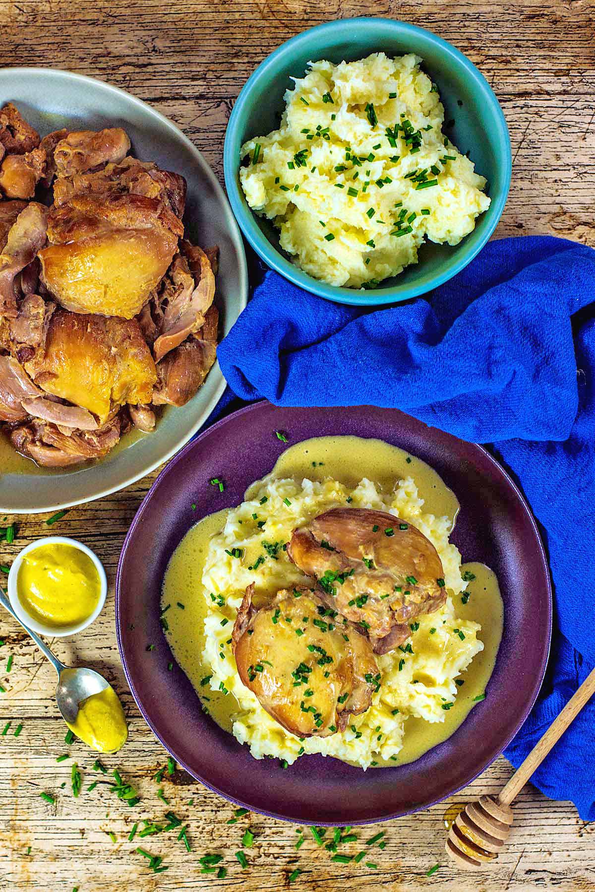 A bowl of cooked chicken thighs and mash potato in a creamy sauce next to bowls of more chicken and mashed potato.